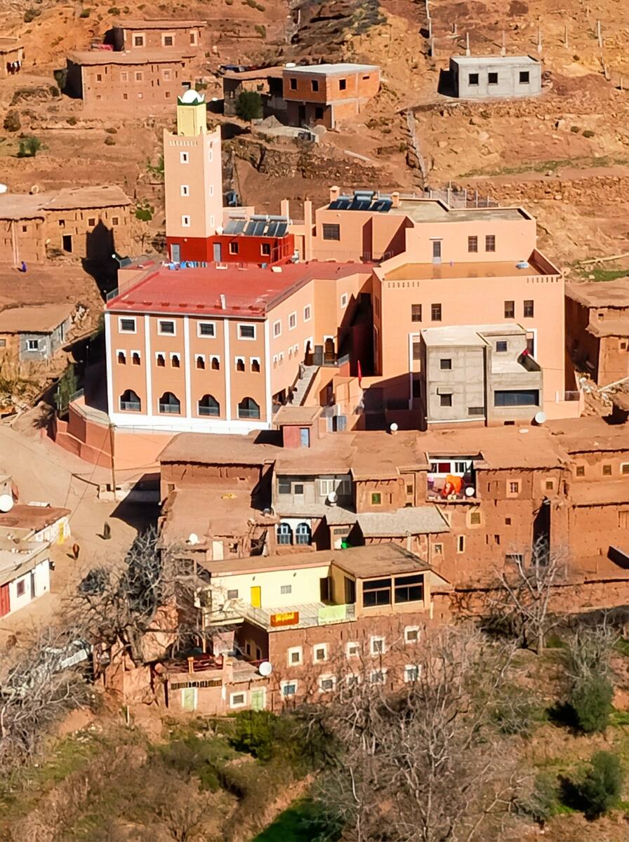 Le gîte Tizi Noubadou en bas de la photo avec plusieurs fenêtres aux contours blancs, terrasse crème et salon aux grandes fenêtres en aluminium